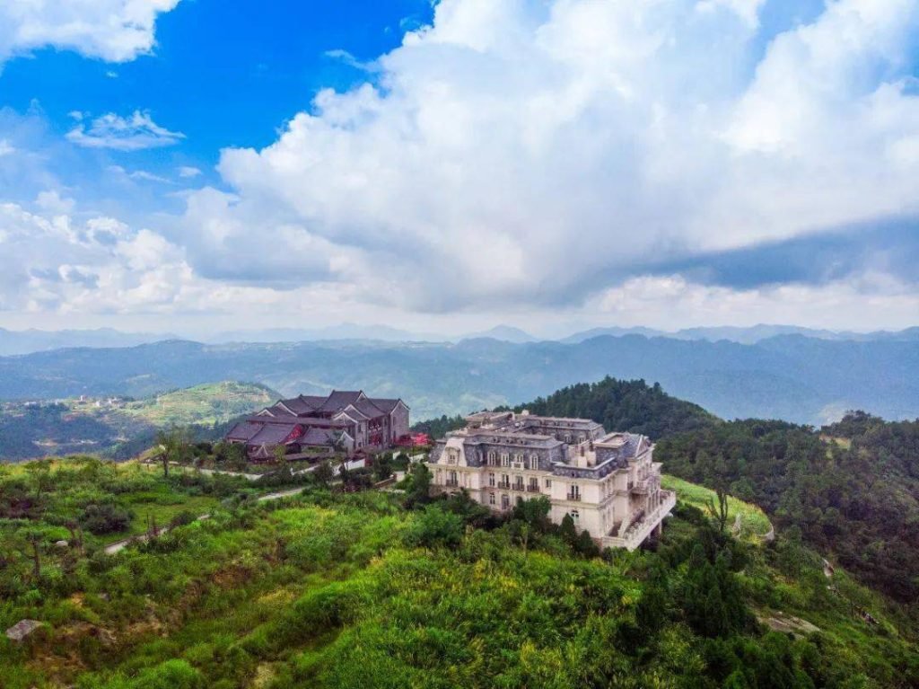 A grand architectural complex overlooking the vast, lush, and rolling green peaks of taishi mountain under a clouded blue sky.